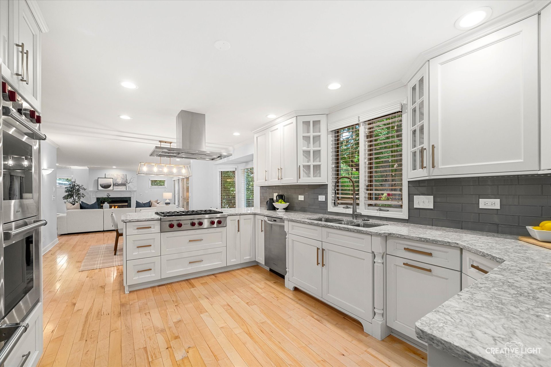Chef’s kitchen at 1101 Barberry Court Downers Grove with white cabinetry, gray tile backsplash, Wolf cooktop, double ovens, and open view to family room.