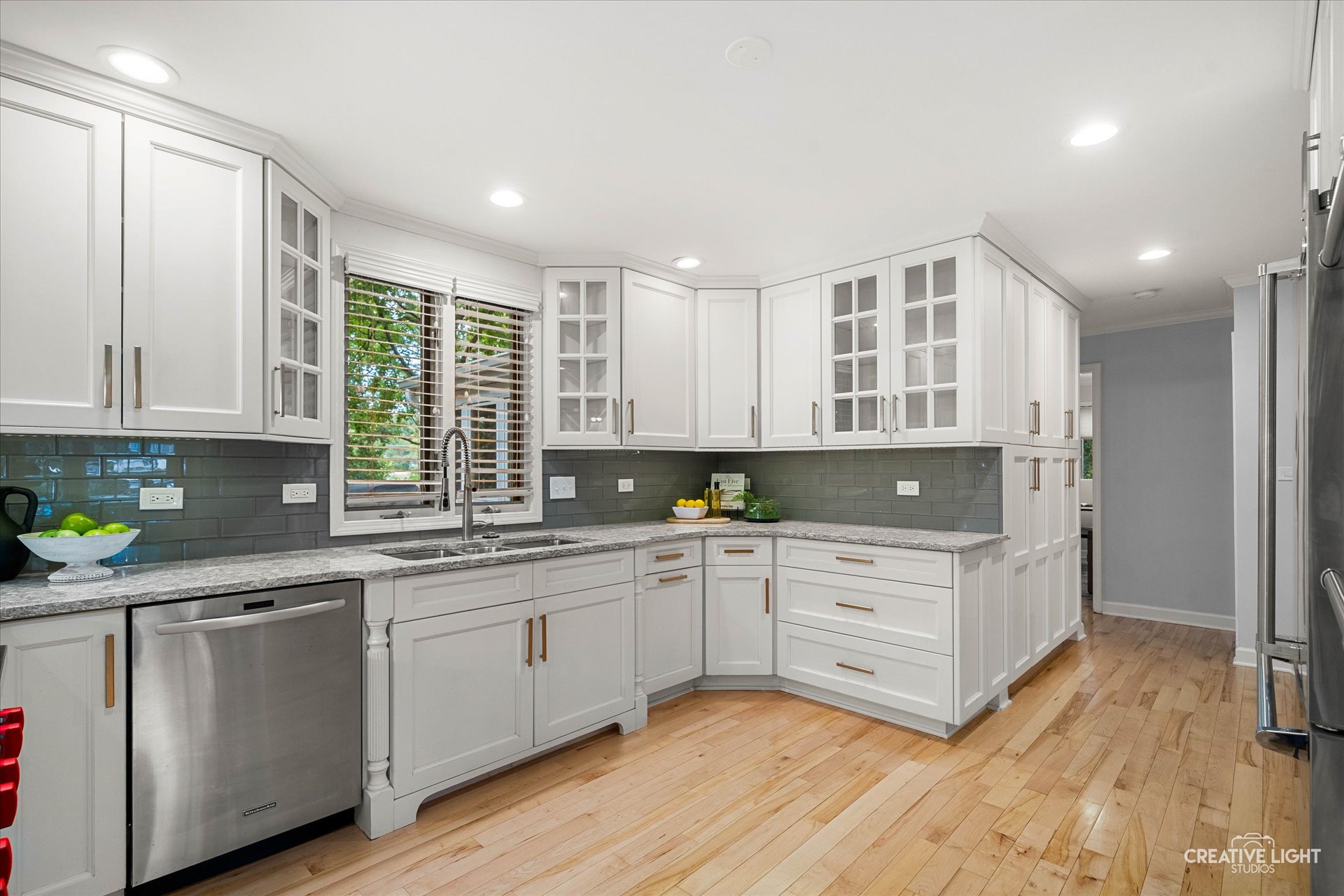 Kitchen at 1101 Barberry Court Downers Grove featuring custom white cabinetry with glass-front doors, gray tile backsplash, brushed gold hardware, and granite countertops.