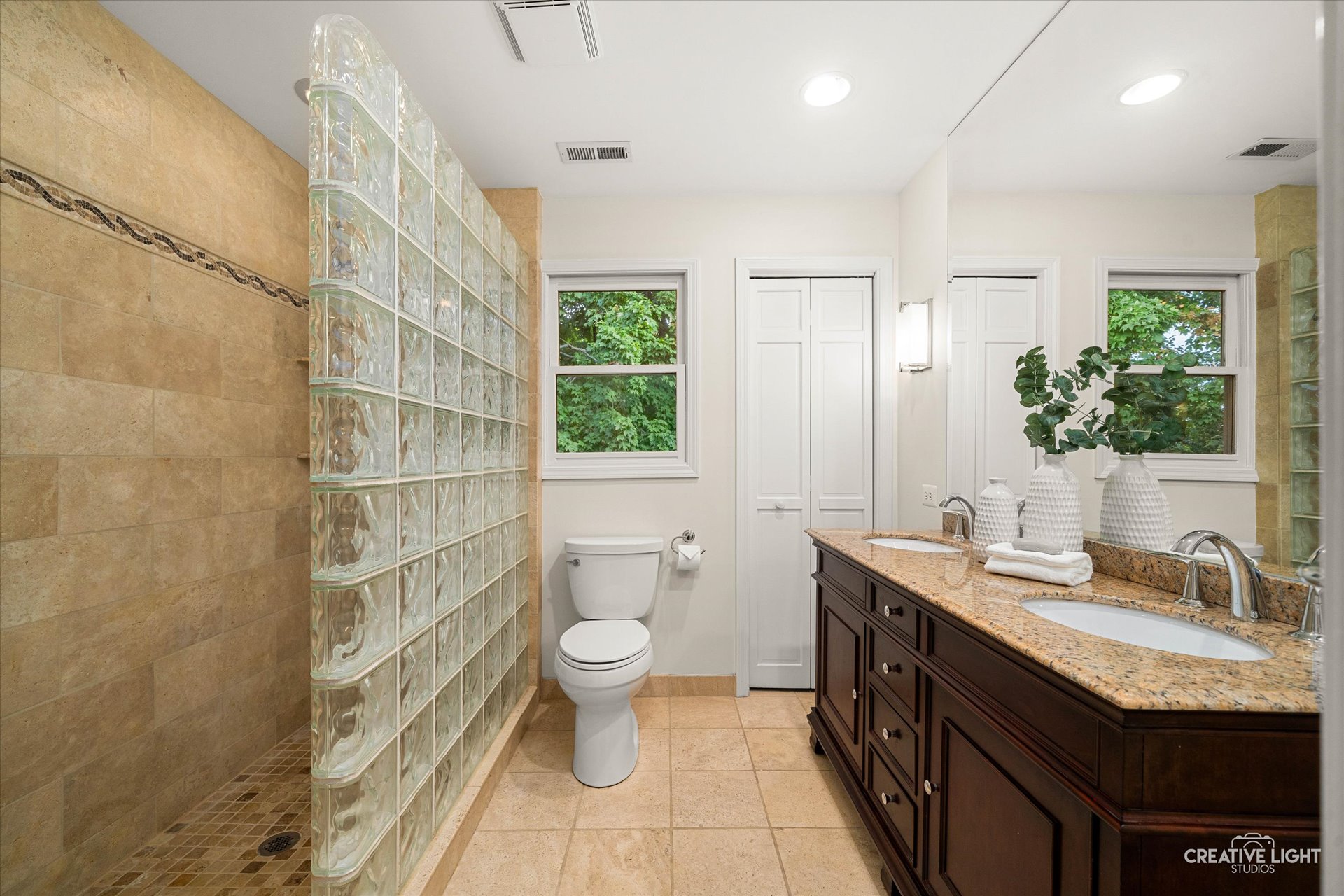 Primary bath at 1101 Barberry Court Downers Grove with glass-block walk-in shower, double vanity with granite countertop, and neutral tile flooring.